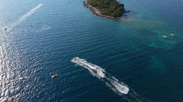 A speedboat races across the clear blue waters of Ksamil, Albania, with swimmers in the distance