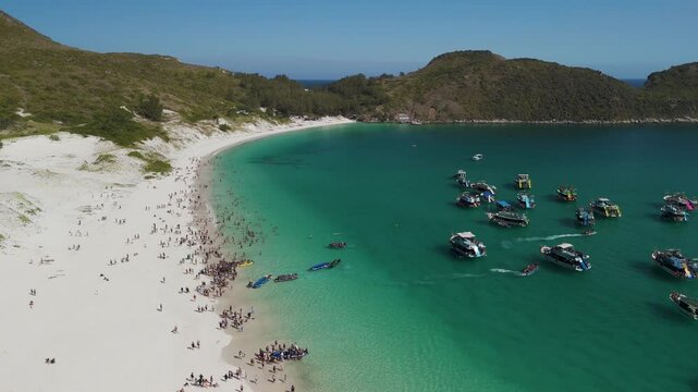 Aerial view of tourists at Parai do Farol pans right toward boats on the water and a strait