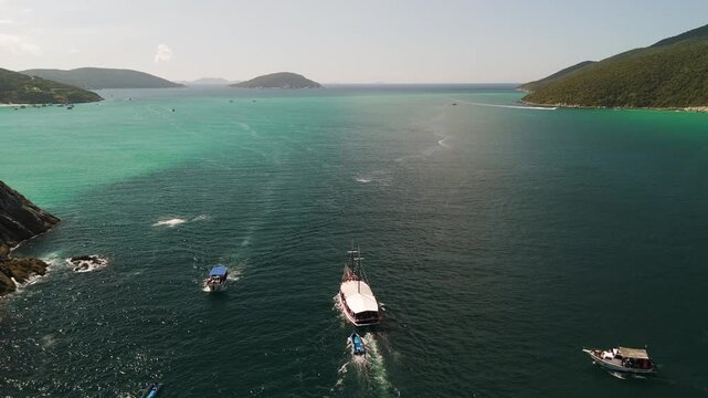 A boat sails on a blue tropical bay on a sunny day in Arrial do Cabo, Brazil, aerial