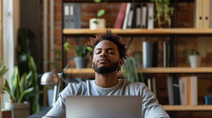 A man sits at his desk with his eyes closed, meditating. He has a laptop in front of him