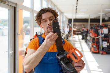 Worker in uniform cheking modern electric chain saw