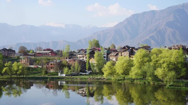 Static shot of a peaceful mountain village by a calm lake with scenic snow-capped peaks.Near the Badam Wari in Srinagar Kashmir. Ideal for nature, travel, and rural landscape content.