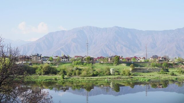 Static shot of a peaceful mountain village by a calm lake with scenic snow-capped peaks.Near the Badam Wari in Srinagar Kashmir.Ideal for nature, travel, and rural landscape content.
