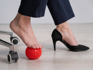 Business woman massages her feet on a massage ball with spikes.