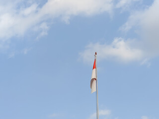 A vibrant red and white Indonesian flag flutters proudly against a canvas of blue sky and fluffy clouds.