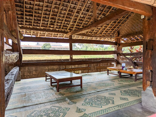 In this close-up, a cozy seating area in a restaurant with a "lesehan" concept invites relaxation. The open walls reveal a stunning wooden framework.