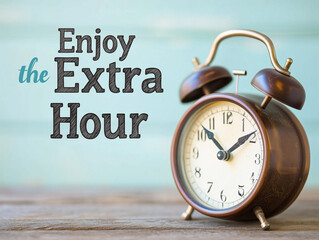 Vintage alarm clock with "Enjoy the Extra Hour" message, light blue wooden background with copy space