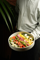 Waiter holding plate with Cobb salad. Healthy cobb salad with bacon, avocado, tomato, eggs and cheese