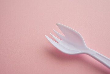 Close up white plastic spork (fork plus spoon) on pink background with copy space. Abstract multi...