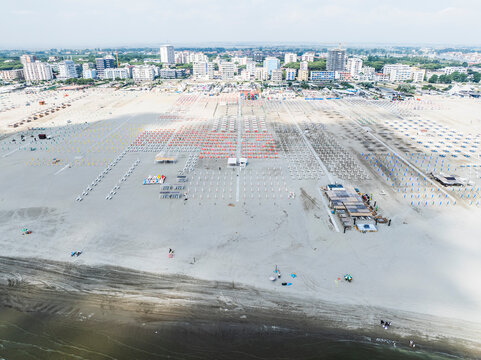 Aerial images of beach full of lounges in perfect arrangement with town in the background. Lido degli Esters, Italy
