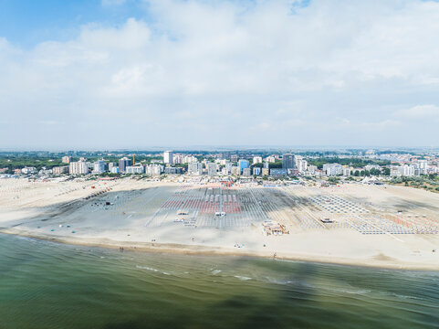 Aerial images of beach full of lounges in perfect arrangement with town in the background. Lido degli Esters, Italy