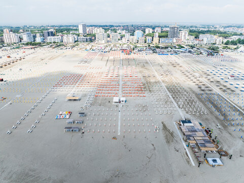 Aerial images of beach full of lounges in perfect arrangement with town in the background. Lido degli Esters, Italy