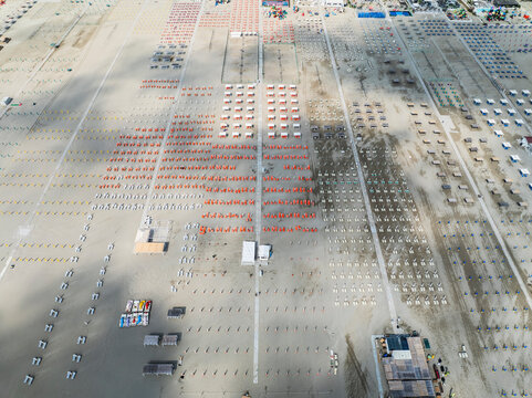 Aerial images of beach full of lounges in perfect arrangement with town in the background. Lido degli Esters, Italy