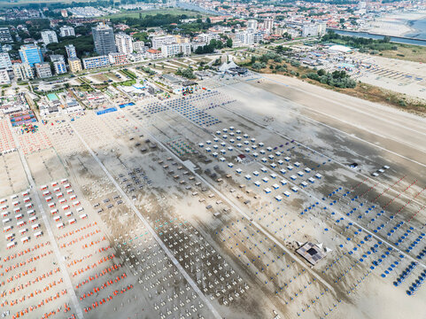 Aerial images of beach full of lounges in perfect arrangement with town in the background. Lido degli Esters, Italy