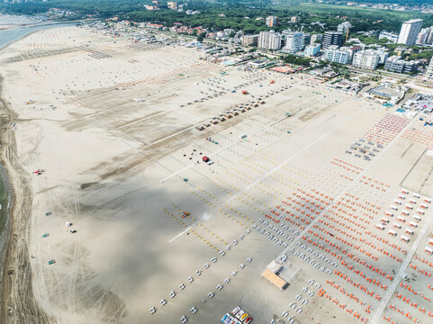 Aerial images of beach full of lounges in perfect arrangement with town in the background. Lido degli Esters, Italy