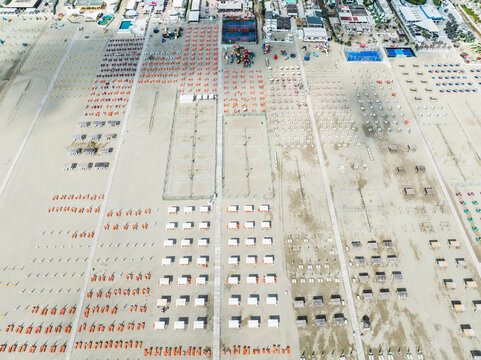 Aerial images of beach full of lounges in perfect arrangement with town in the background. Lido degli Esters, Italy