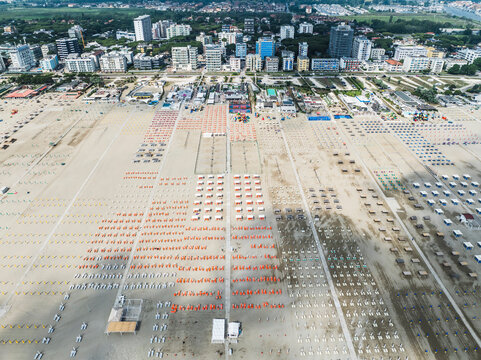 Aerial images of beach full of lounges in perfect arrangement with town in the background. Lido degli Esters, Italy
