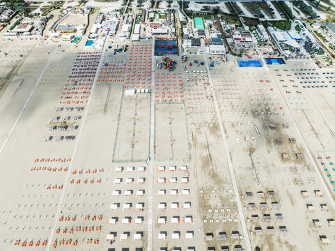 Aerial images of beach full of lounges in perfect arrangement with town in the background. Lido degli Esters, Italy