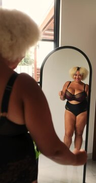 Young African American curvy plus size woman dancing in front of mirror in lingerie and admiring her reflection. Self love and acceptance, positive attitude towards body. Seductive female body.