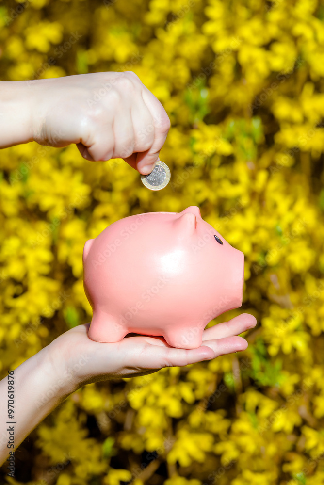 Wall mural girl holding piggy bank against the background of blossoming forsythia