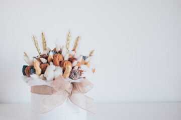 Obraz premium Beautiful handmade Christmas bouquet of nuts, pinecones and cotton flowers in round gift box against white background. Holiday floral decor. Copy space for text.