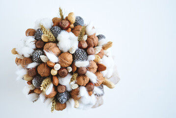 Obraz premium Beautiful handmade Christmas bouquet of nuts, pinecones and cotton flowers, top down view on white background. Holiday floral decor. Copy space for text.