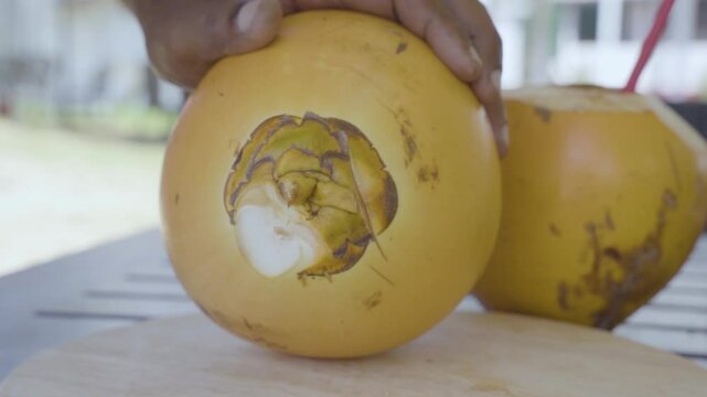 A king coconut being rotated and expertly cut, revealing its refreshing interior from multiple angles. The footage highlights the intricate process of opening the tropical fruit.