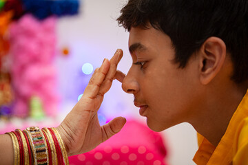 An Indian woman applying tilak on forehead after completing a Hindu pooja, symbolizing devotion and blessing rituals.