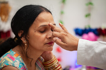 An Indian man applying tilak on forehead after completing a Hindu pooja, symbolizing devotion and...