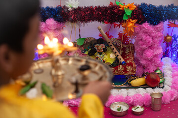 An Indian boy is ready to perform aarti, a Hindu religious ritual, in the background of an Indian Hindu puja.