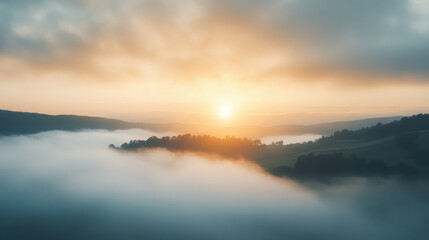 Fototapeta premium A serene sunrise breaking through morning fog over rolling hills creates tranquil atmosphere. soft light illuminates landscape, evoking sense of peace and calm