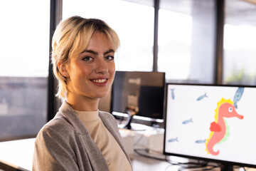 Smiling woman in office with computer displaying colorful seahorse animation