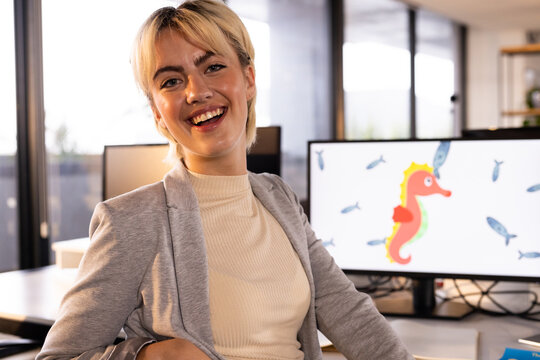 Smiling woman in office with computer displaying seahorse and fish illustration