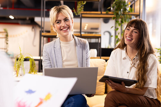 Discussing creative writing business, smiling women using laptop and tablet in office