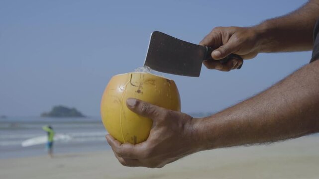 A king coconut is expertly sliced open on the sandy beach, revealing the fresh, hydrating water inside. The scene captures the vibrant colors of the coconut and the relaxed, sunlit atmosphere.