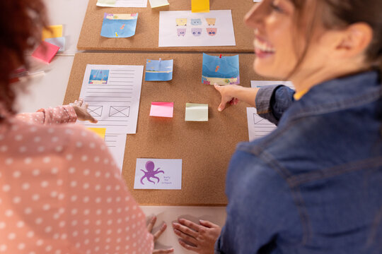 At office, collaborating on creative project, multiracial women using sticky notes and corkboard