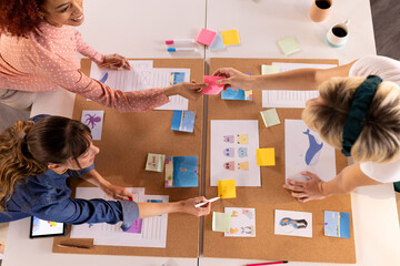 At office, collaborating on creative project, multiracial women using sticky notes and illustrations