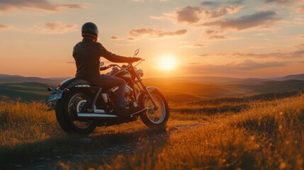 A lone motorcyclist sits on their bike overlooking a mountain range with a sunset in the background.