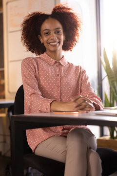 Smiling woman sitting at desk in office, wearing polka dot shirt