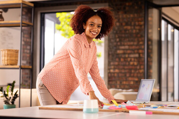 Smiling woman organizing colorful sticky notes on desk in creative office