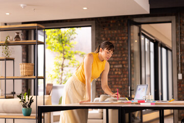 Writing notes on desk, woman in yellow top working in modern office