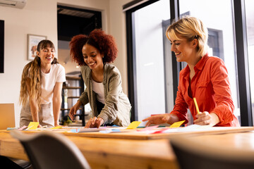 At office, multiracial women brainstorming and writing ideas on sticky notes