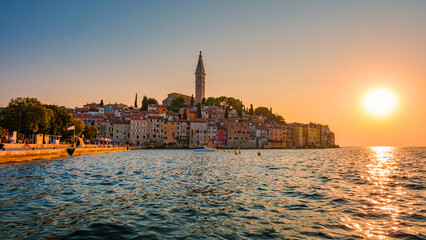 Obraz premium As the sun sets over Rovinj, vibrant buildings line the waterfront, their colors illuminating the tranquil water. The warm glow of dusk creates a magical atmosphere in this coastal gem.