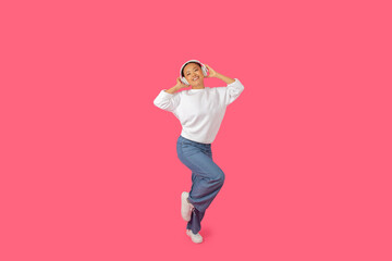 Asian young woman in casual attire dances happily, expressing joy and enthusiasm with her headphones on in a bright setting.