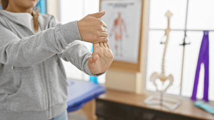A hispanic woman performs wrist exercises indoors at a rehab clinic, displaying focused healthcare.