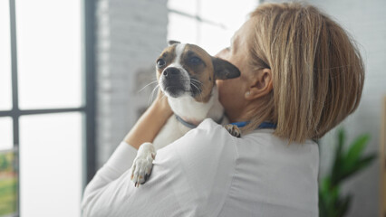 A middle-aged blonde woman holds a small dog in a veterinary clinic, showcasing the bond between a pet and its caretaker.