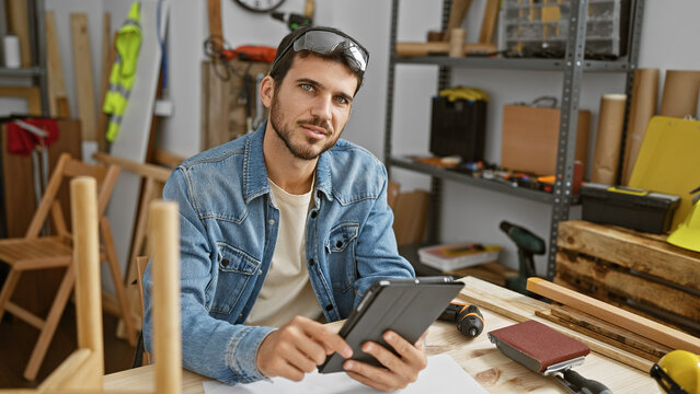 Handsome bearded craftsman using a tablet in a creative carpentry workshop