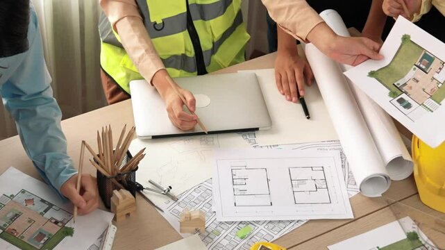 Smart architect and safety engineer discussion about building blueprint on table with architectural document, measurement tools and wooden block scatter around at modern office. Closeup. Delineation.