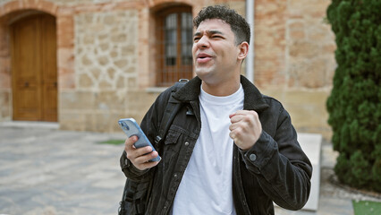 Fototapeta premium A young man holds his phone with a puzzled expression on an ancient city street.