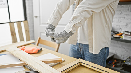 A man assembles wooden frames in a bright carpentry workshop, illustrating craftsmanship and manual labor.